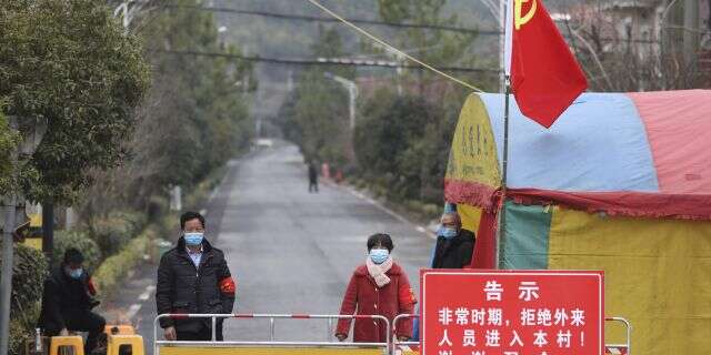 Volunteers stand beneath a Communist Party flag as they man a barricade checkpoint at a village in Hangzhou in eastern China's Zhejiang Province, Monday, Feb. 3, 2020. (Chinatopix via AP)