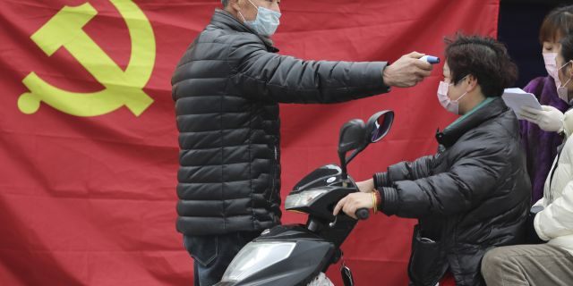A volunteer stands in front of a Communist Party flag as he takes the temperature of a scooter driver at a roadside checkpoint in Hangzhou in eastern China's Zhejiang Province, Monday, Feb. 3, 2020. China sent medical workers and equipment to a newly built hospital, infused cash into financial markets and further restricted people's movement in sweeping new steps Monday to contain a rapidly spreading virus and its escalating impact. (Chinatopix via AP)